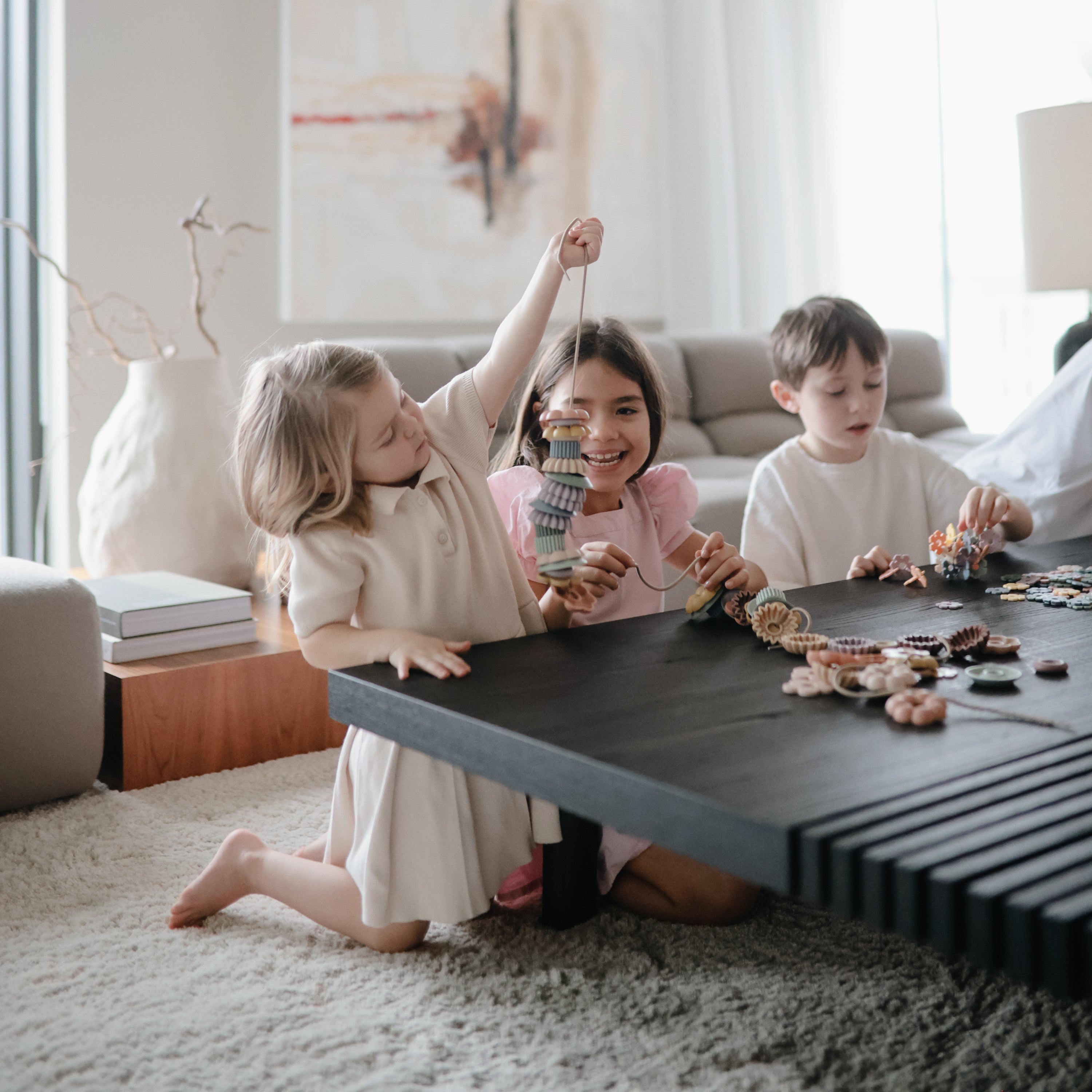 Enfants enfilant les perles du jeu de laçage Mushie dans le salon