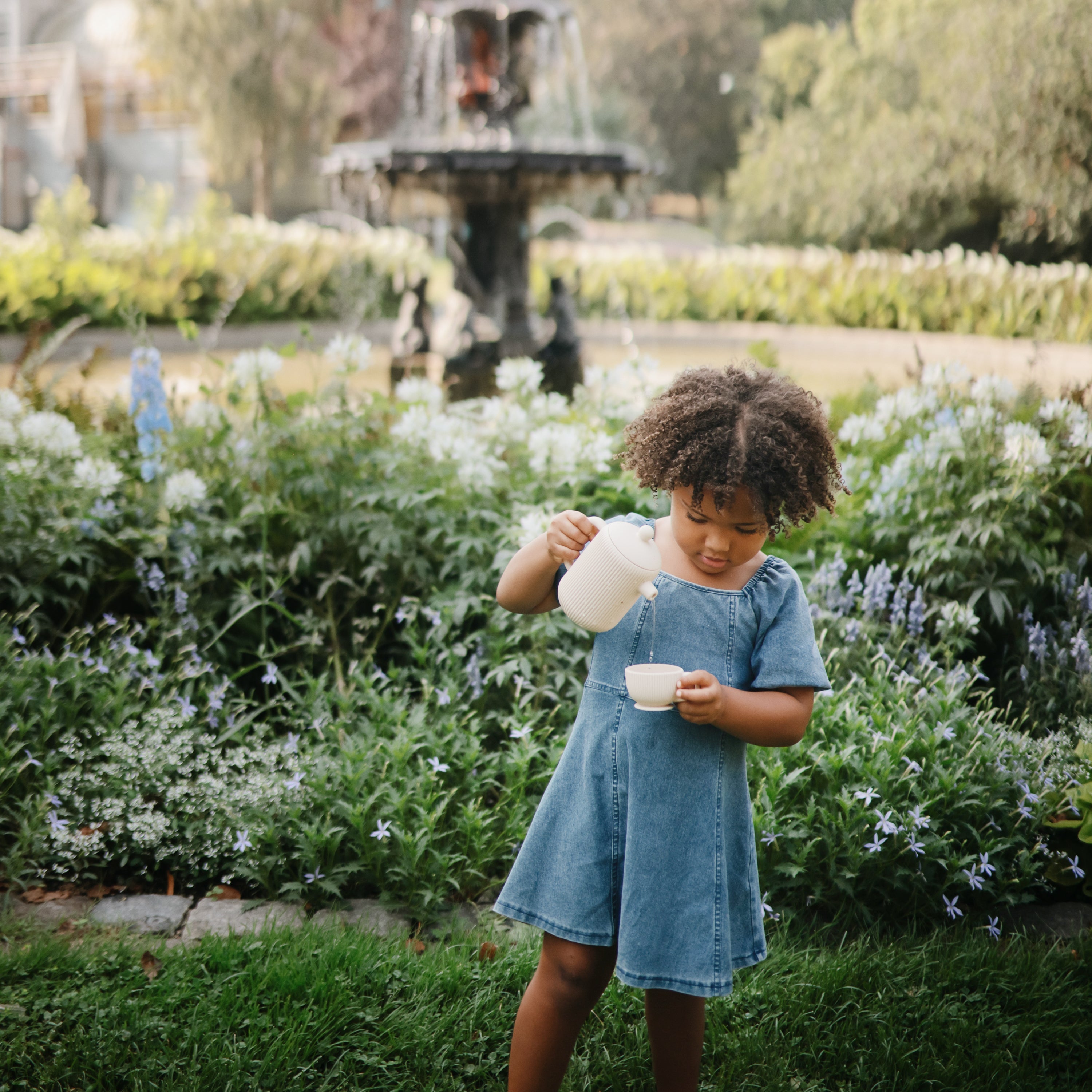 Petite fille versant de l'eau avec la théière Mushie dans un jardin