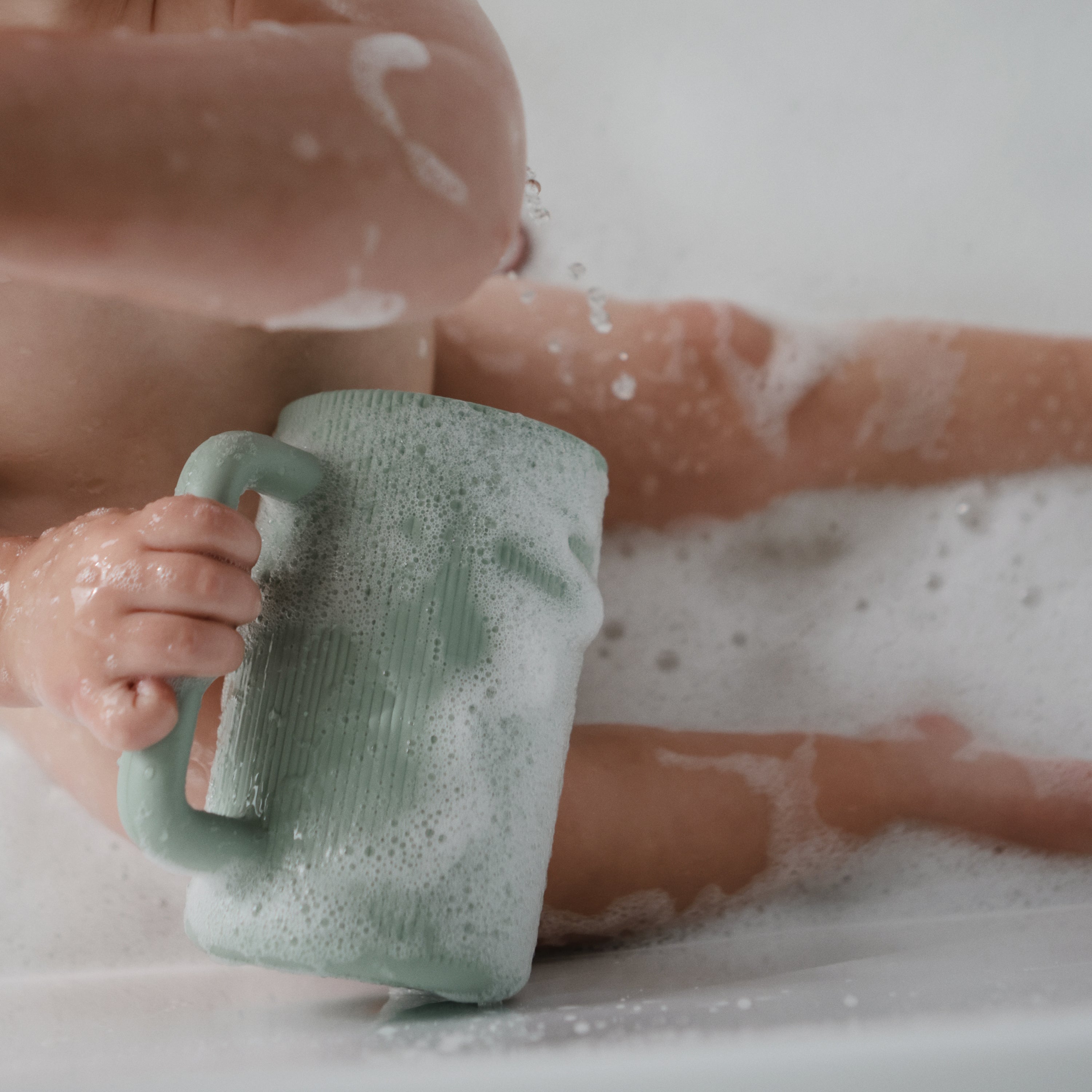 Bébé tenant le gobelet de rinçage Mushie dans le bain