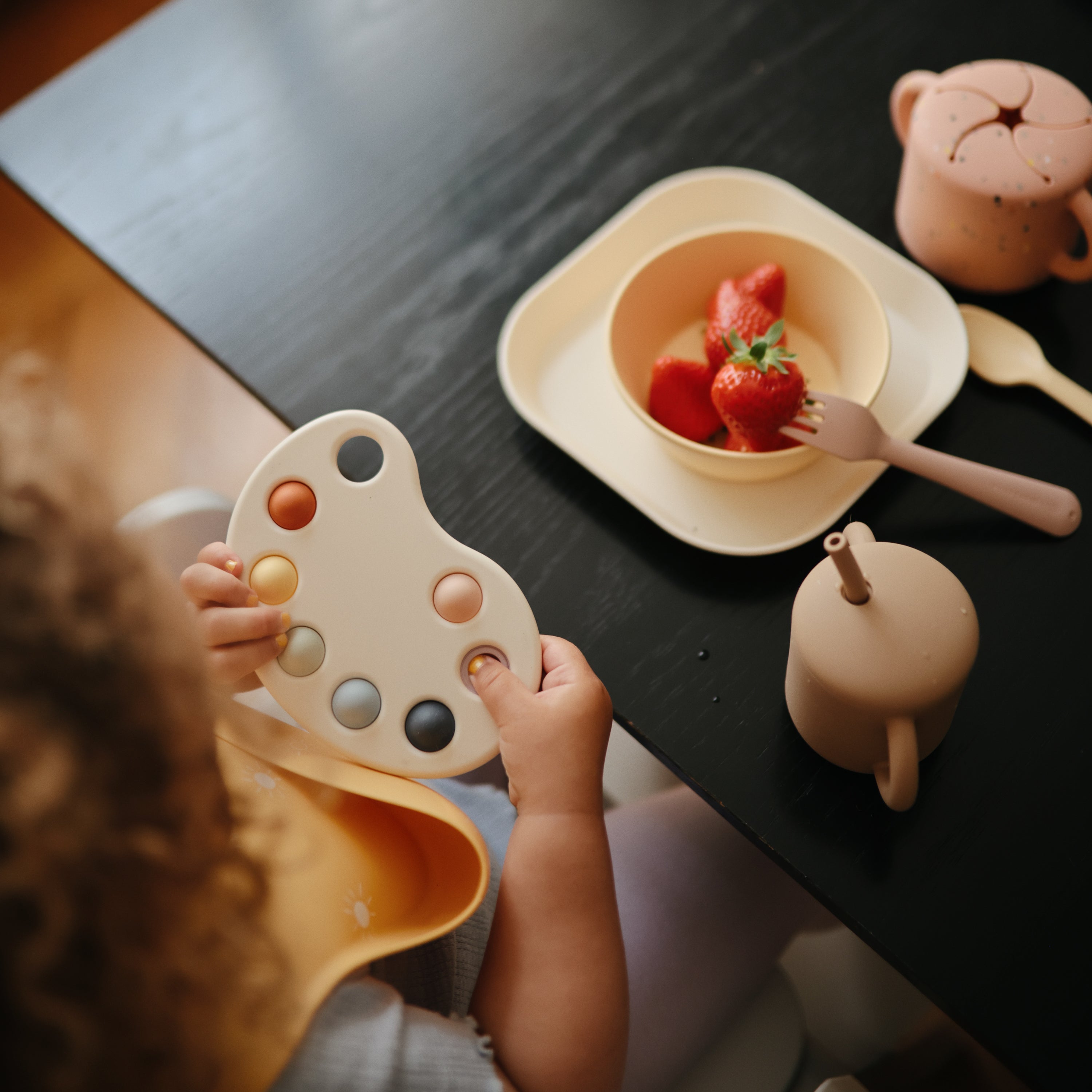 Enfant à table avec le jouet à presser Mushie