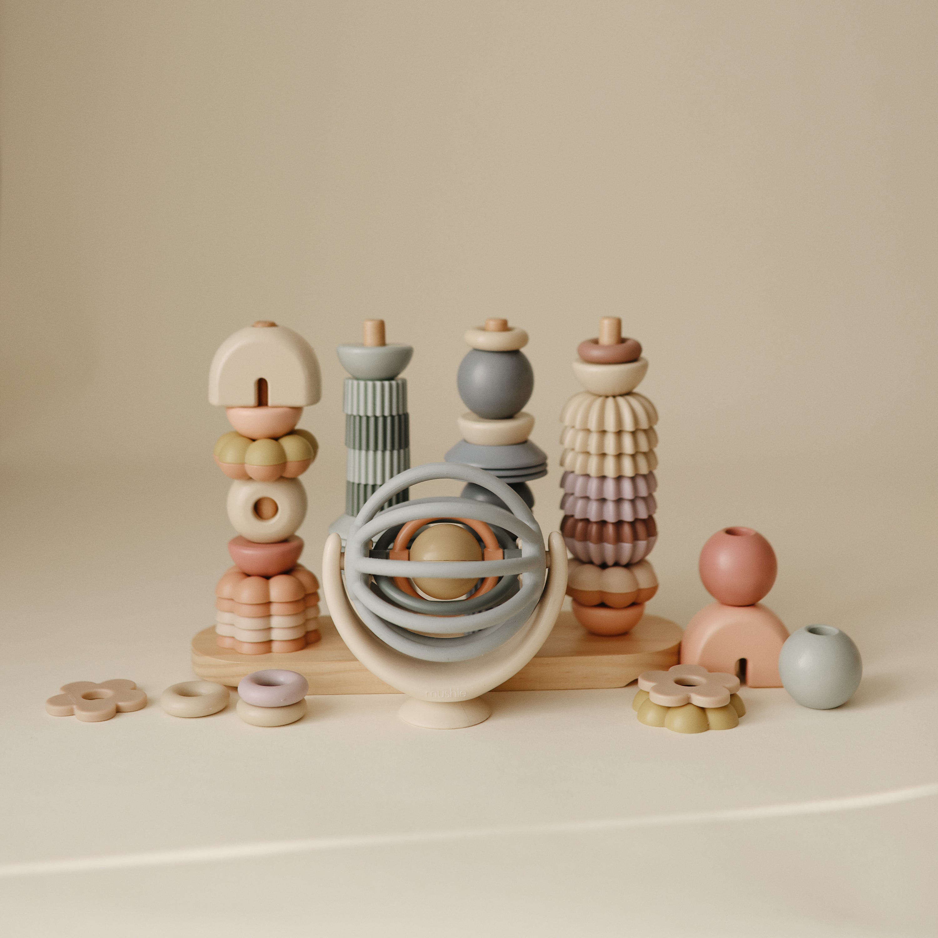 Toupie Balle Mushie et jouets en bois pastel disposés sur fond beige