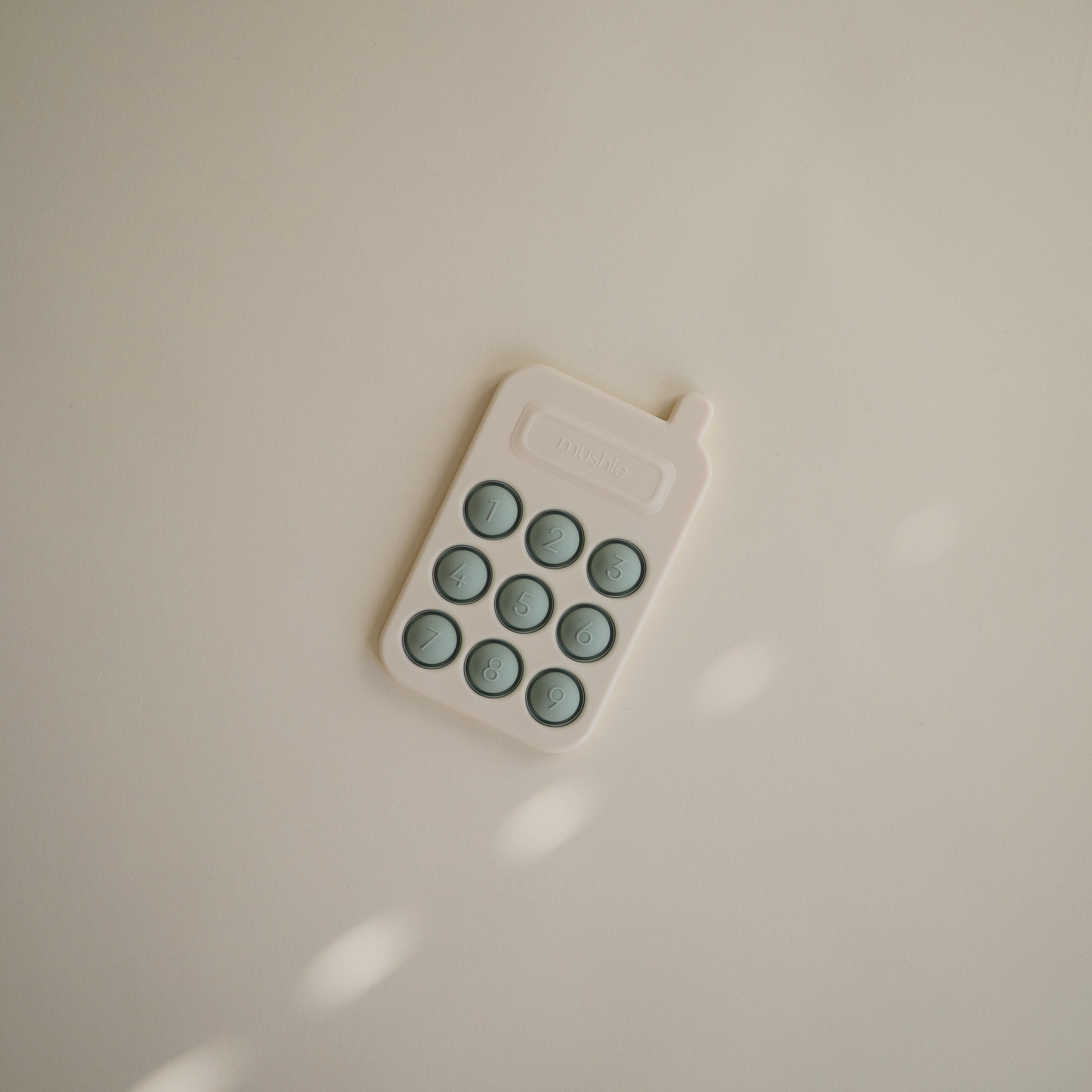 Téléphone à presser Mushie posé sur fond neutre