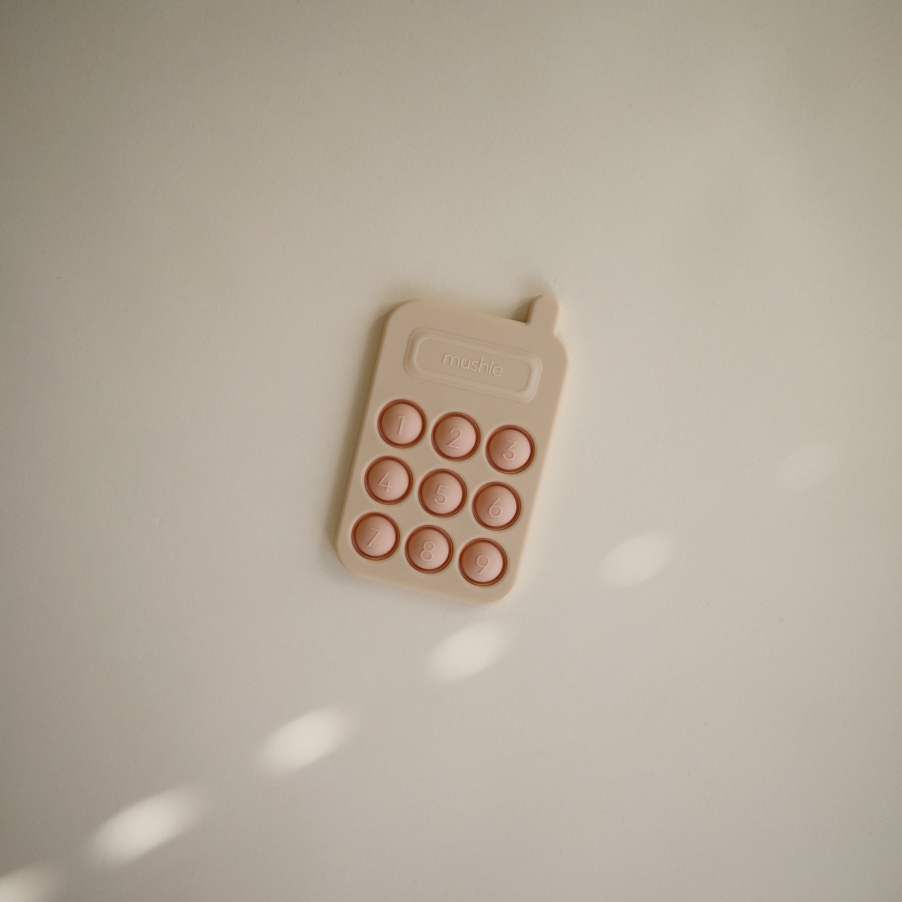 Téléphone à presser Blush Mushie posé sur fond neutre