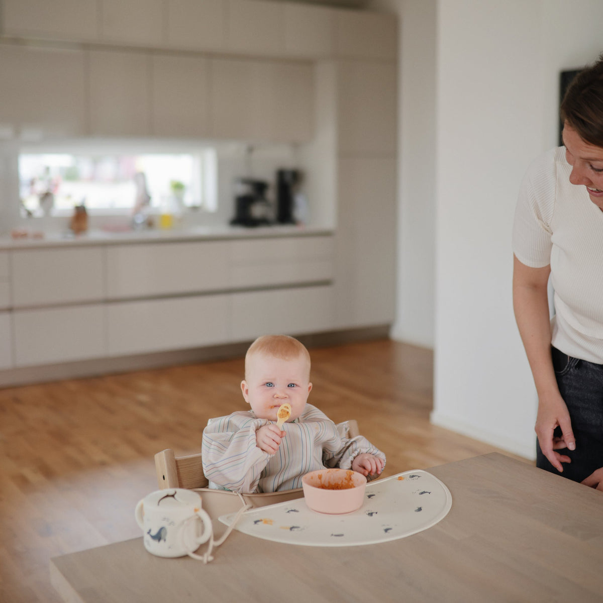 Bébé grignotant dans son gobelet à goûter Mushie sur la chaise haute