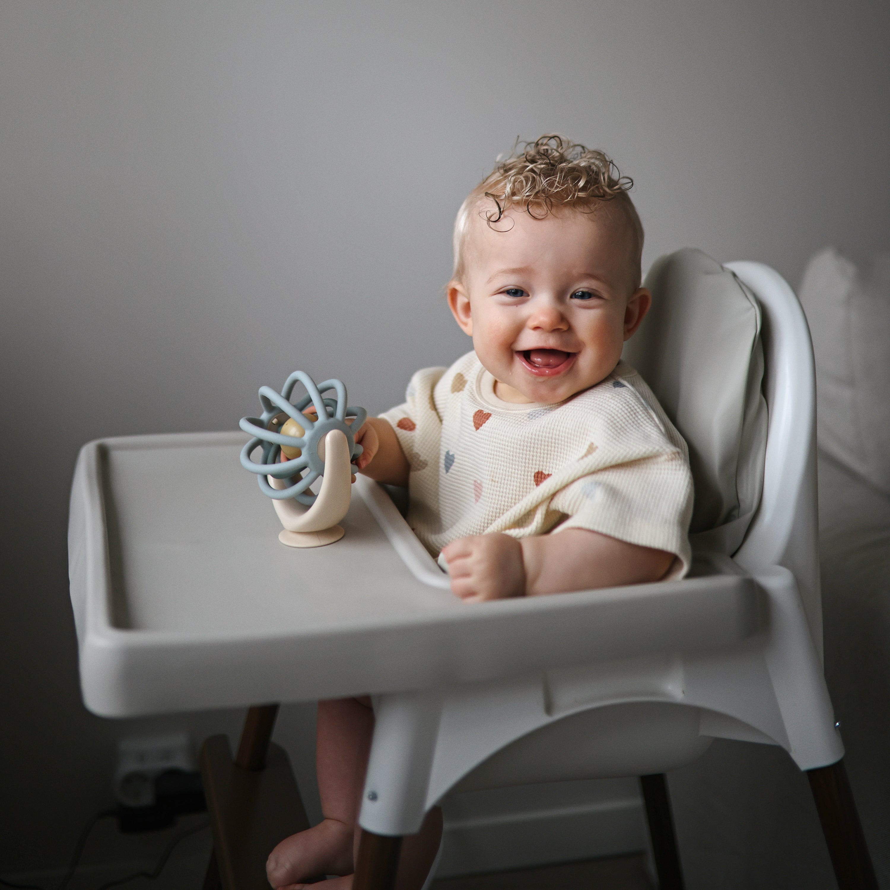 Bébé souriant en chaise haute devant la toupie Balle Mushie fixée à la tablette