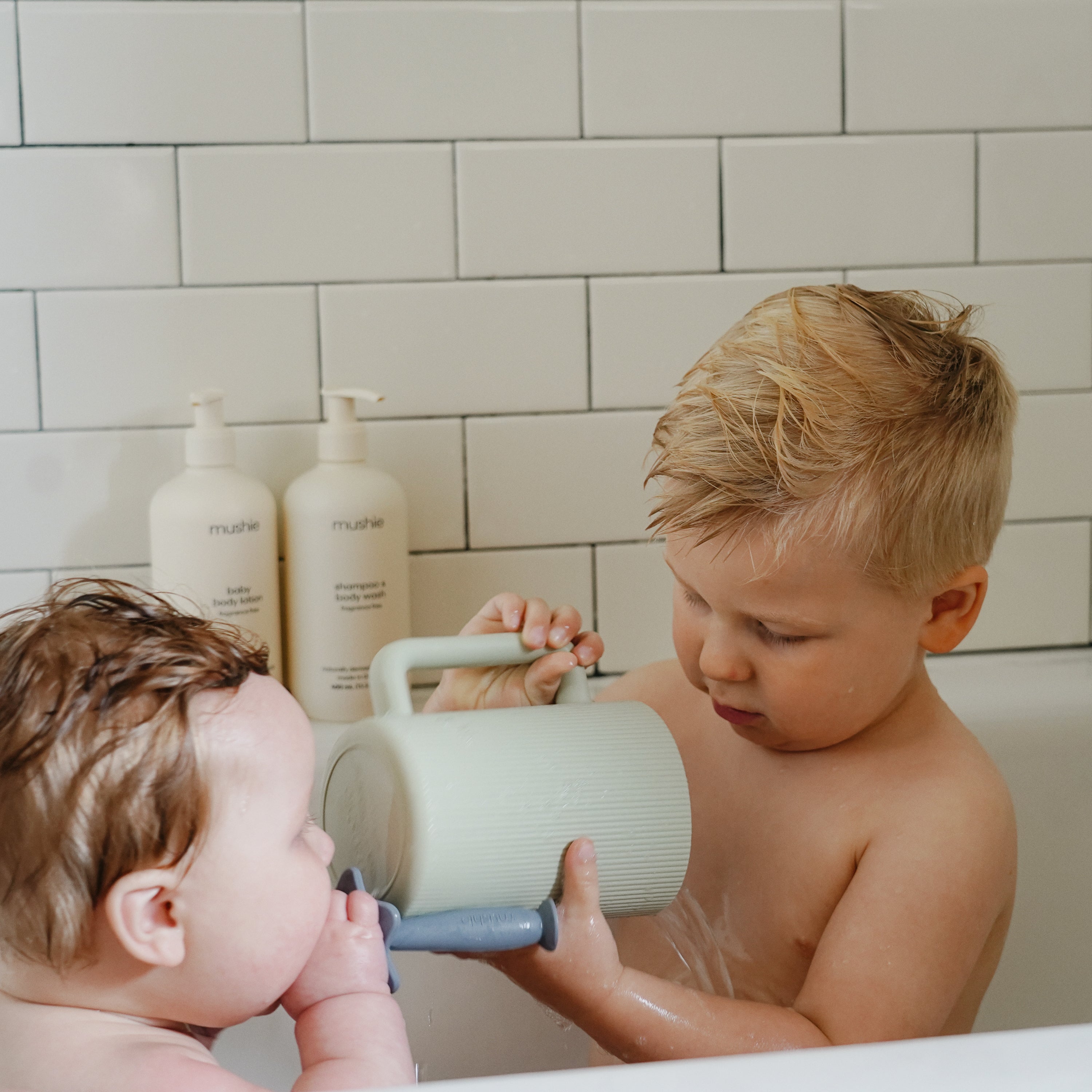 Grand frère versant de l'eau sur la tête de bébé avec le gobelet Mushie