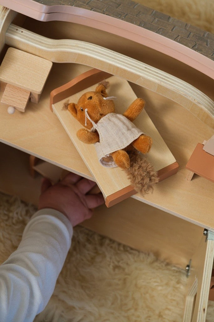 Écureuil en peluche couché dans le lit en bois de la maison de poupées
