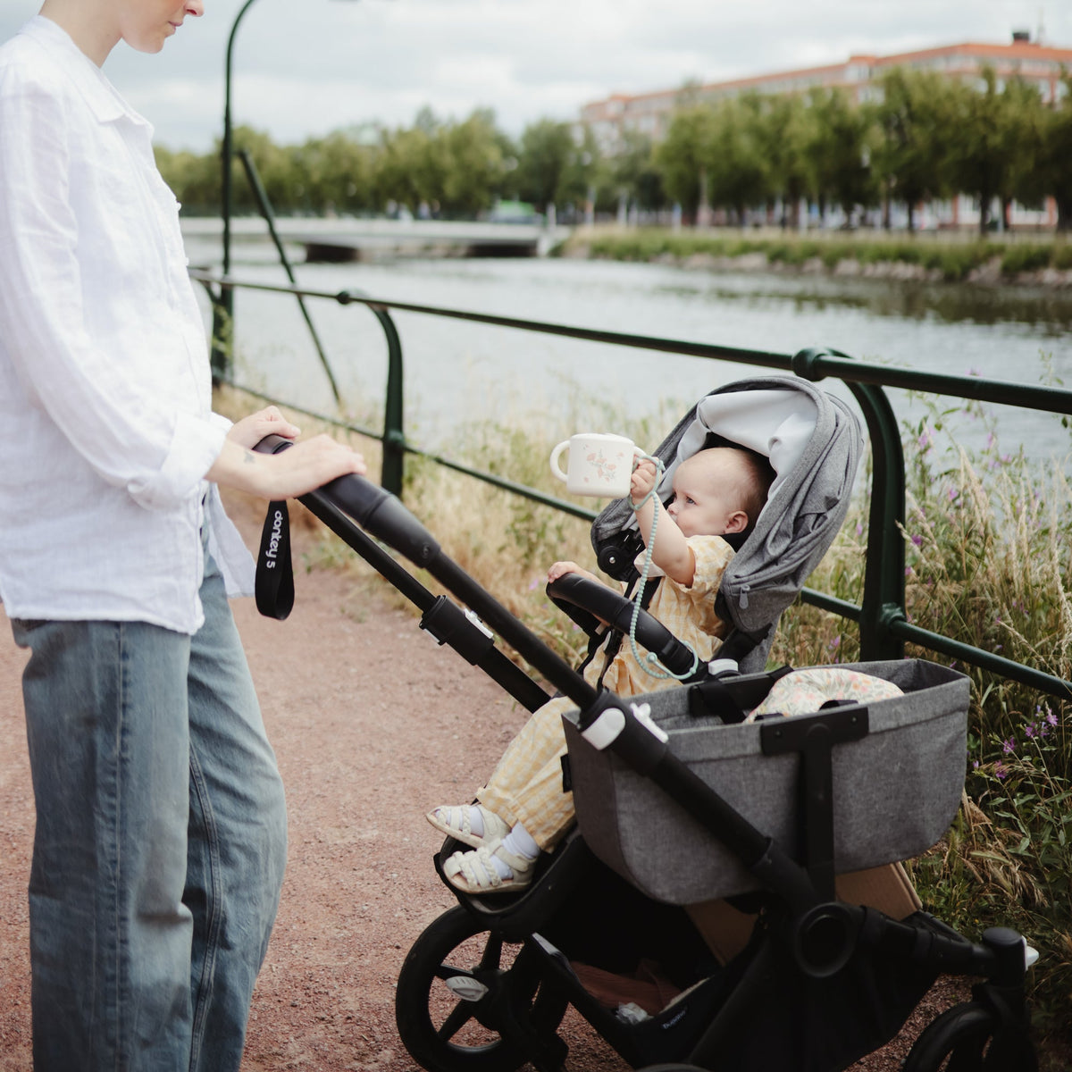 Bébé en poussette tenant son gobelet à goûter Mushie en balade