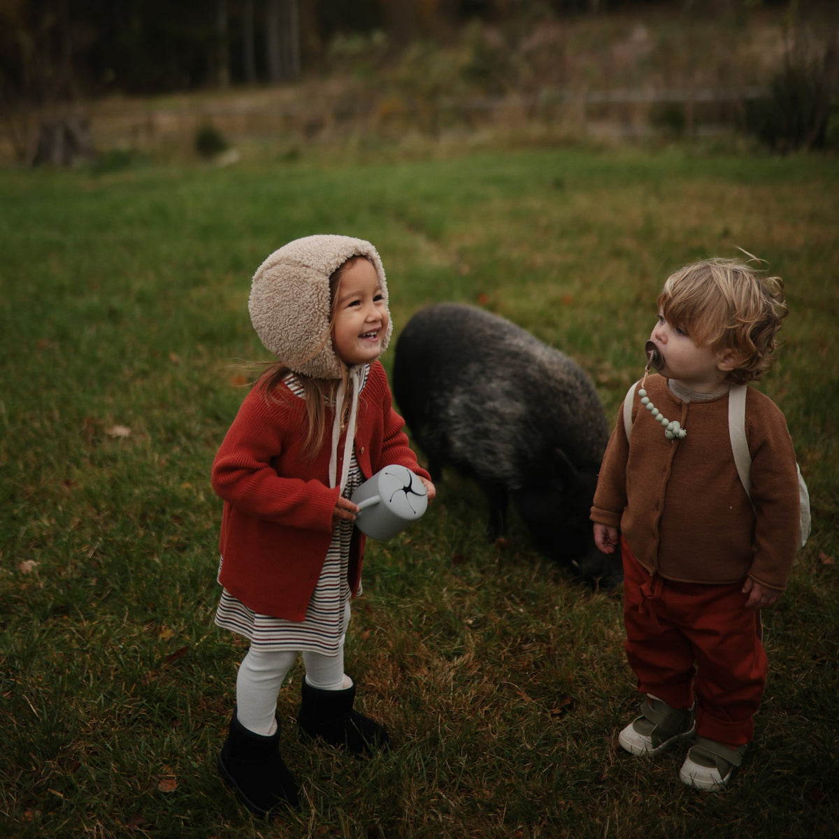 Deux enfants en bottes avec leurs gobelets à goûter Mushie en automne