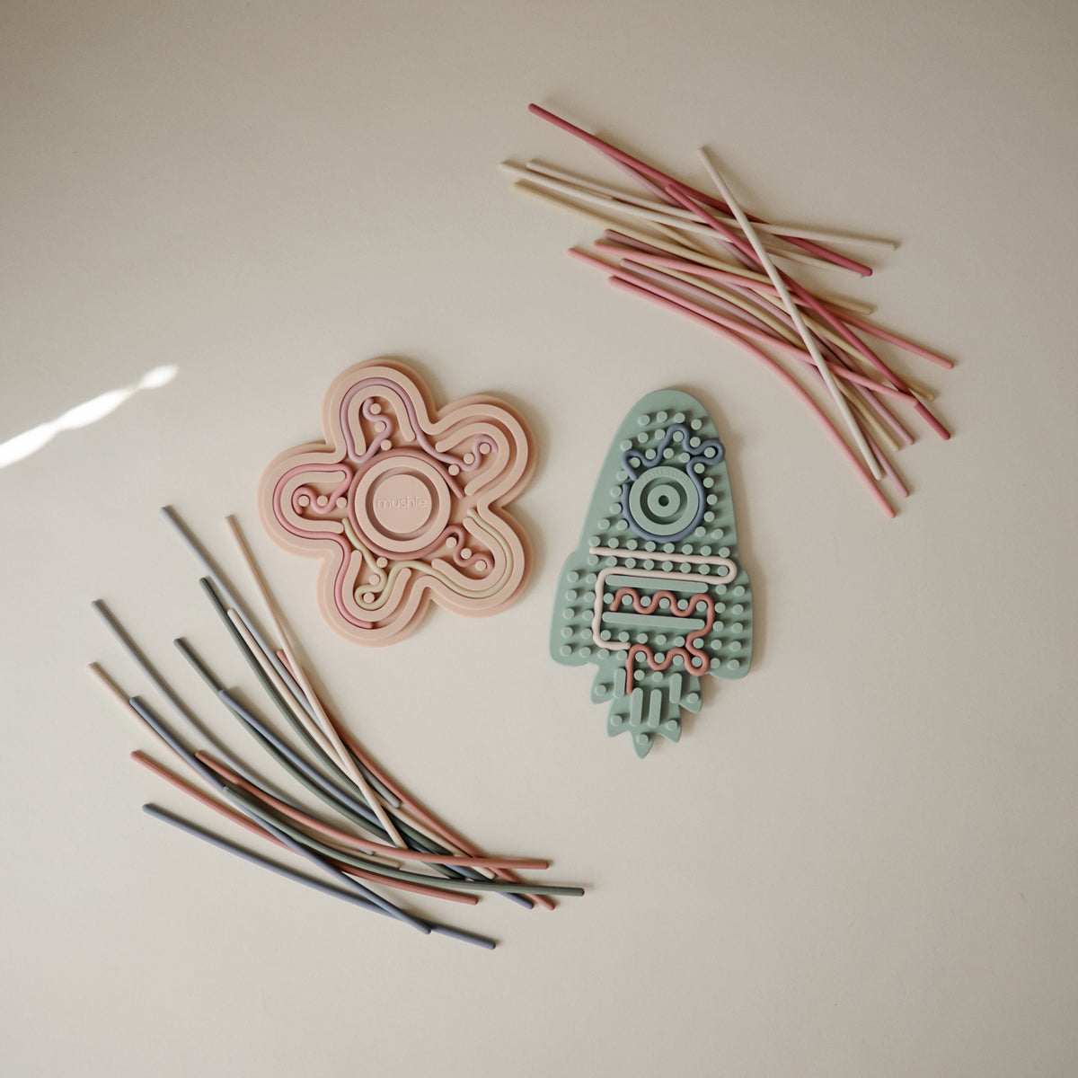 Deux jouets sensoriels Mushie et leurs cordons colorés