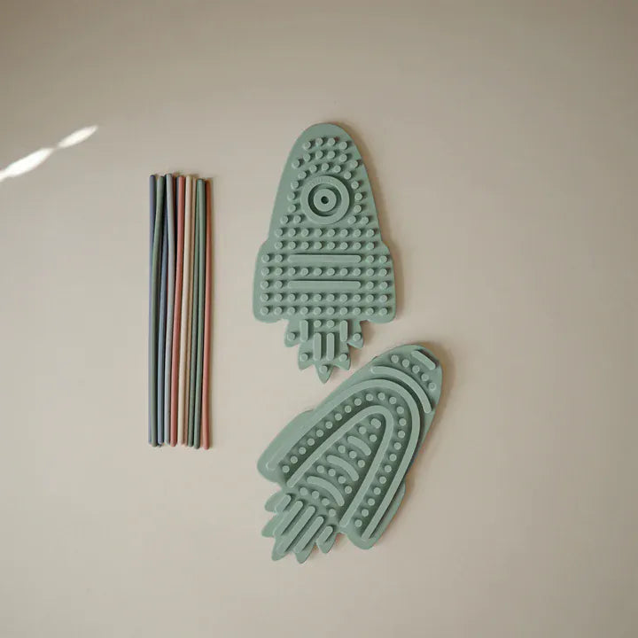 Fusée sensorielle Mushie décorée de cordons de couleur